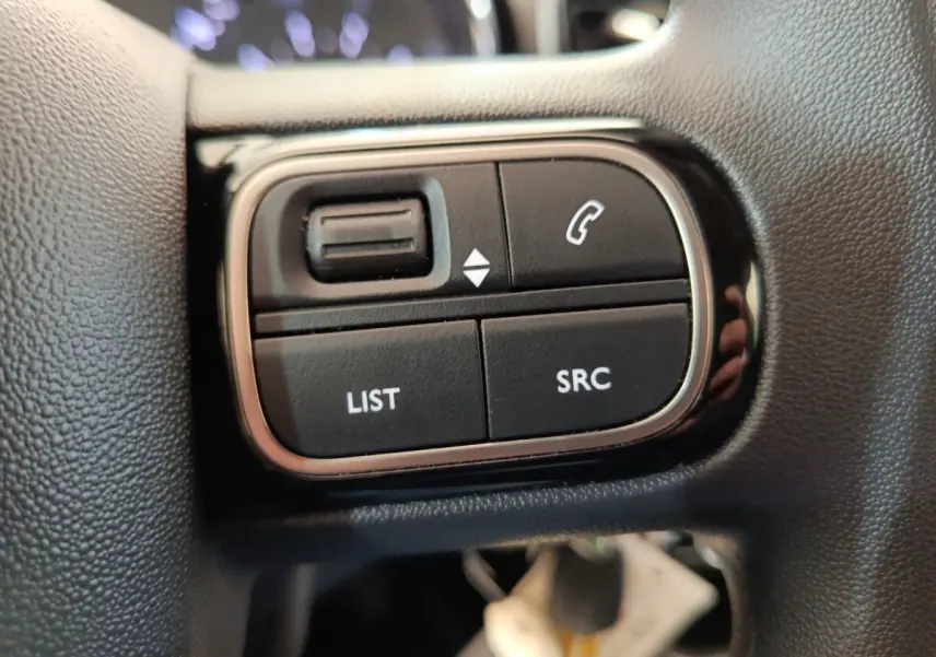 Gros plan sur les commandes au volant noir de la Citroën C3 PureTech 2022, boutons LIST, SRC et téléphone.