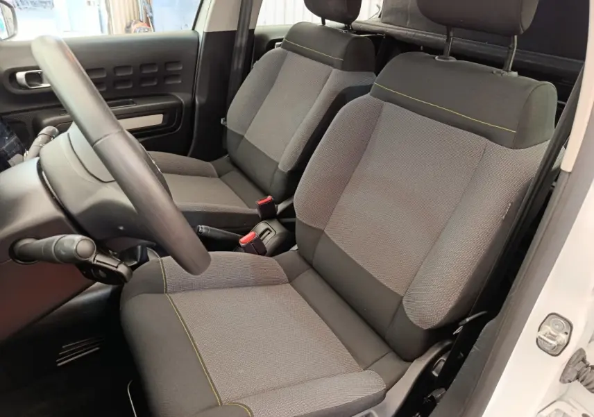 Vue intérieure côté conducteur de la Citroën C3 blanche 2022, sièges tissu gris avec surpiqûres jaunes.