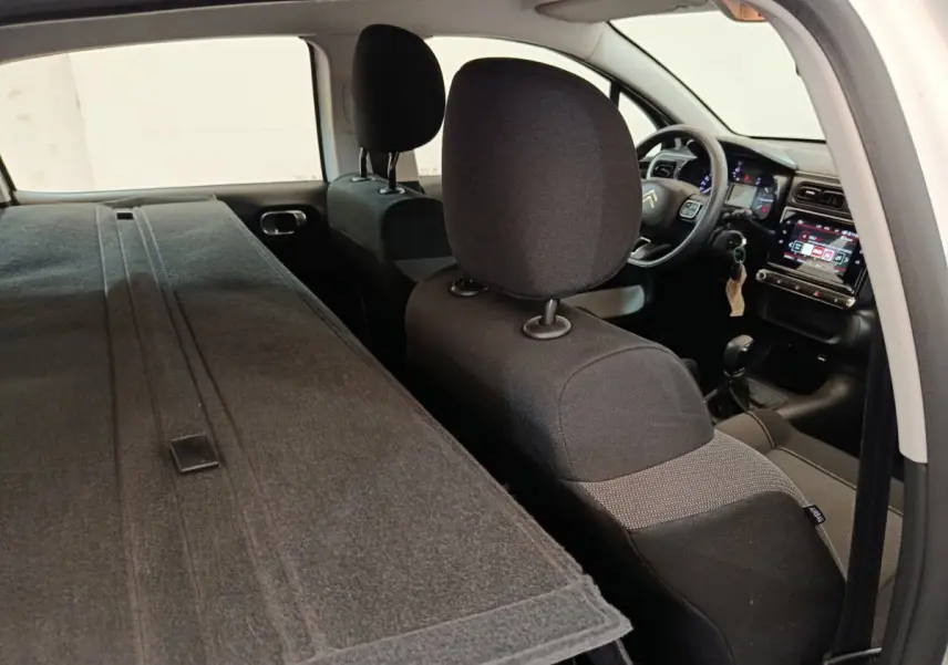 Vue intérieure arrière droite de la Citroën C3 blanche, sièges rabattus et tableau de bord avec écran tactile visible.