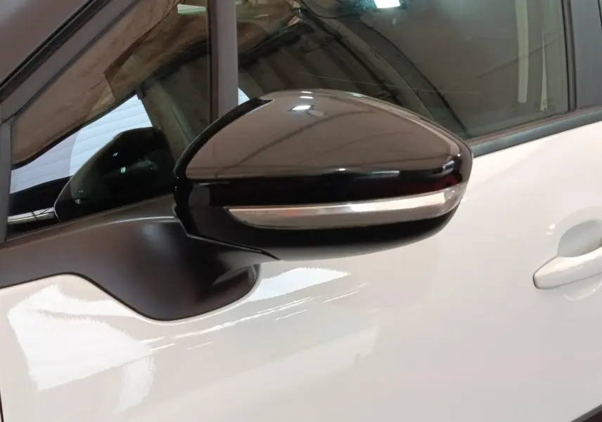 Rétroviseur noir avec clignotant intégré sur porte blanche d'une Citroën C3 PureTech vue de près côté gauche.