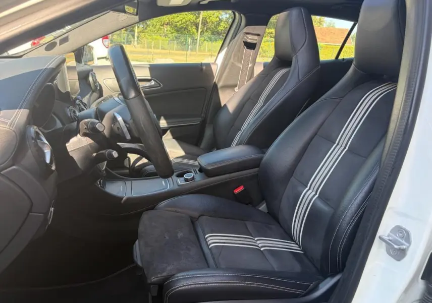 Vue intérieure côté conducteur du Mercedes GLA 220d blanc, mettant en valeur les sièges noirs avec bandes blanches et le tableau de bord.