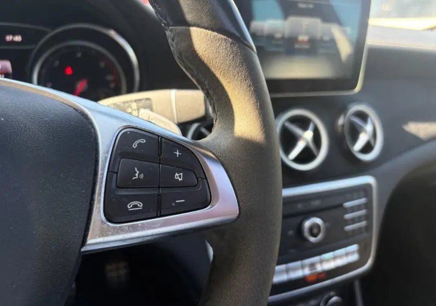 Gros plan sur le volant côté gauche du Mercedes GLA blanc 2017, avec commandes audio et aérateurs ronds en arrière-plan.