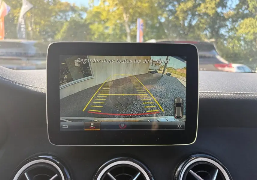 Écran central montrant la caméra de recul avec lignes de guidage dans un Mercedes GLA blanc, vue intérieure avant.