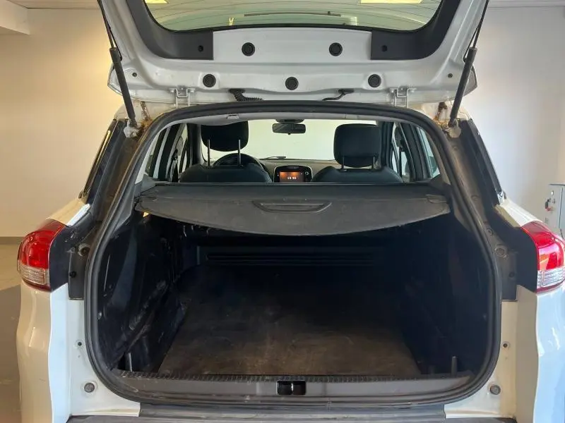 Vue arrière ouverte du coffre d'une Renault Clio Estate blanc glacier, avec tablette cache-bagages et intérieur sombre visible.