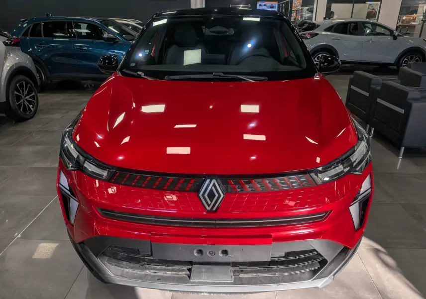 Vue de face du Renault Captur E-TECH 2025 en Rouge Flamme avec toit noir dans un showroom.