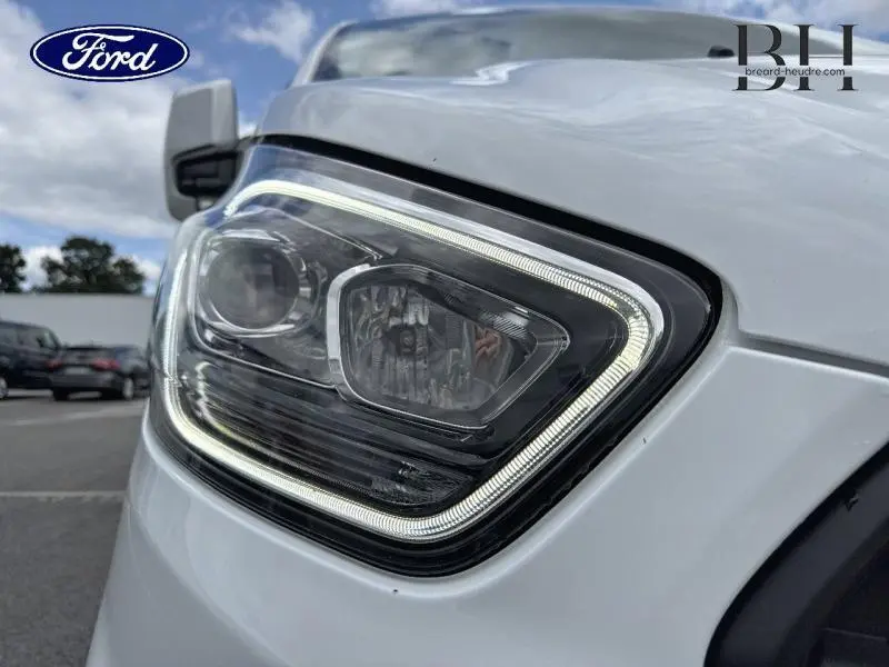 Gros plan sur le phare avant droit du Ford Transit Custom blanc Glacier 2023 avec éclairage LED en forme de contour lumineux.