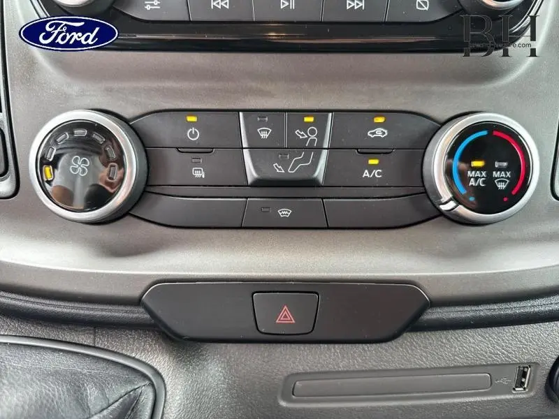 Gros plan sur les commandes de climatisation et ventilation du Ford Transit Custom blanc Glacier, avec boutons rétroéclairés et réglages activés.