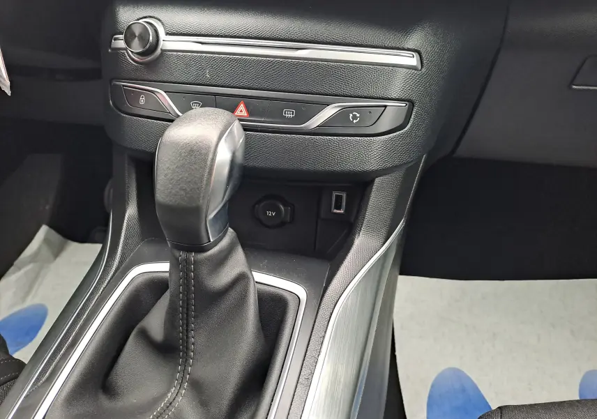 Gros plan sur la commande de boîte automatique en cuir noir et plastique argenté dans une Peugeot 308 gris 2019.