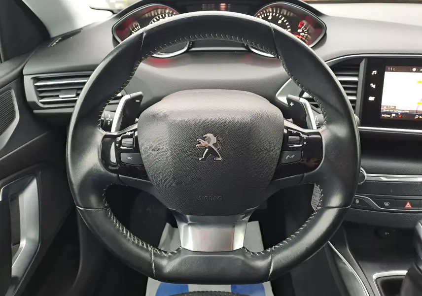 Vue rapprochée du volant en cuir noir de la Peugeot 308 2019 avec commandes intégrées et tableau de bord visible.