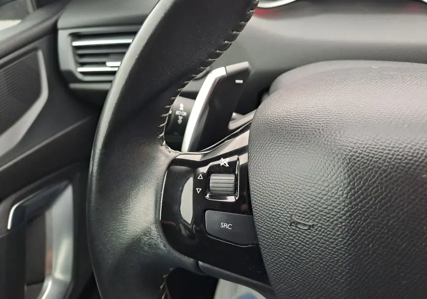 Gros plan sur le volant noir de la Peugeot 308 gris, mettant en valeur les commandes audio intégrées côté gauche.