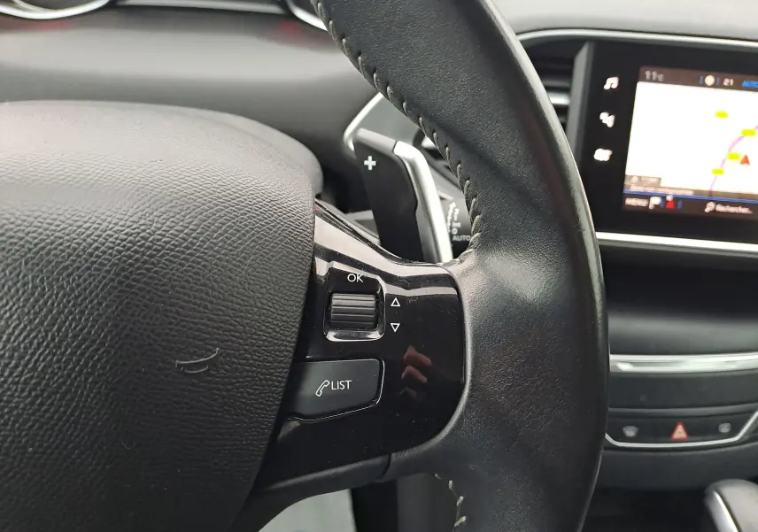 Gros plan sur le volant en cuir noir de la Peugeot 308 2019 avec commandes intégrées et écran tactile du tableau de bord.