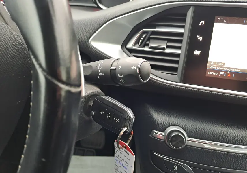 Gros plan sur le volant et la clé insérée du Peugeot 308 gris, avec l'écran tactile et la commande d'essuie-glace visibles.