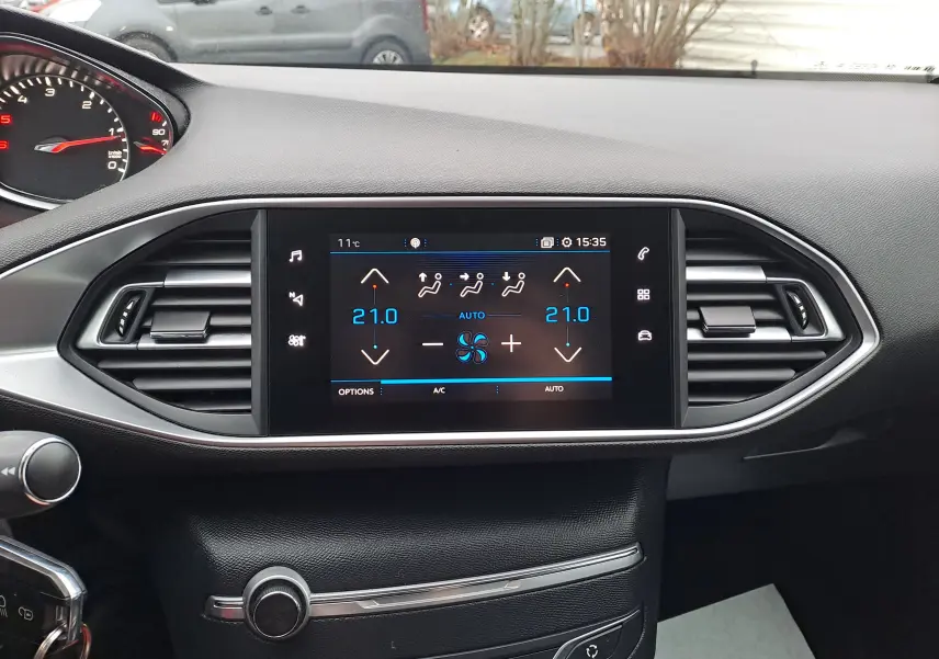 Tableau de bord intérieur de Peugeot 308 gris, vue frontale sur l'écran tactile de climatisation digitale à 21°C.