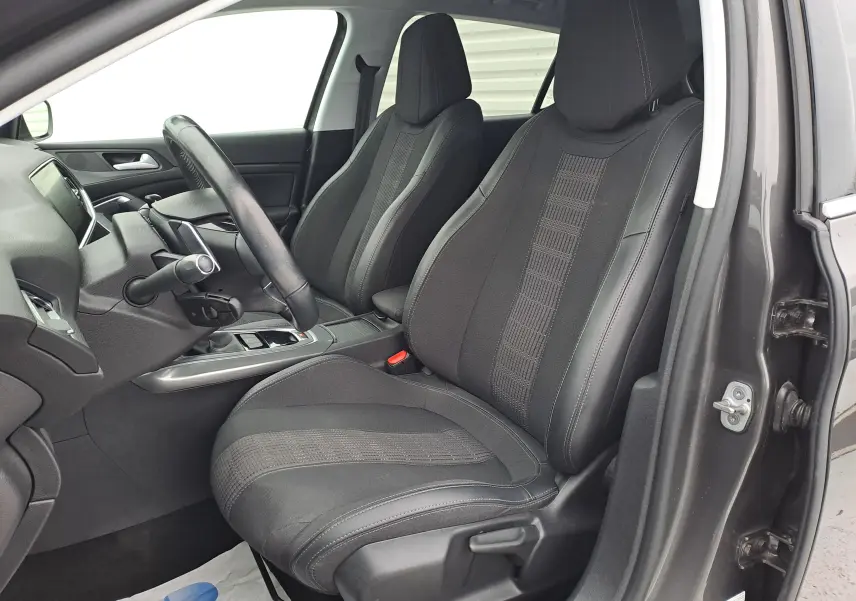 Vue intérieure côté conducteur de la Peugeot 308 gris 2019, sièges noirs en tissu et cuir avec volant multifonction.