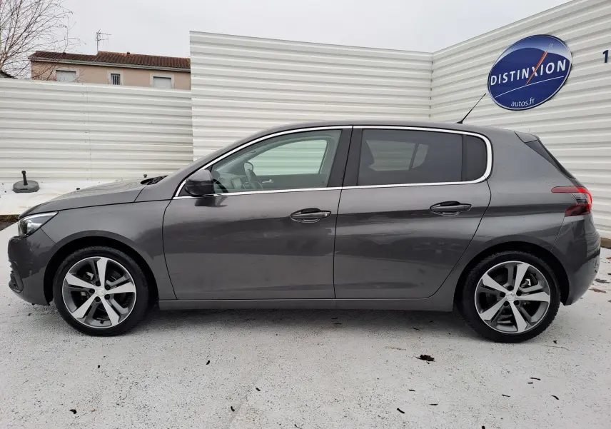 Peugeot 308 gris vue de profil côté gauche, avec jantes alliage bicolores et vitres teintées.