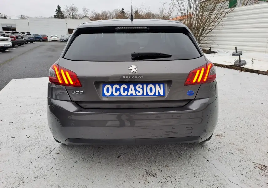 Vue arrière d'une Peugeot 308 gris foncé avec feux allumés et plaque d'immatriculation "OCCASION" visible.