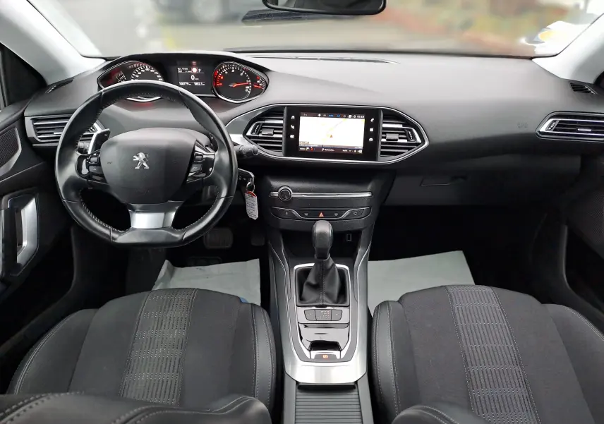 Vue intérieure avant de la Peugeot 308 1.5 BlueHDi 130ch Allure avec tableau de bord noir et écran tactile central affichant la navigation.