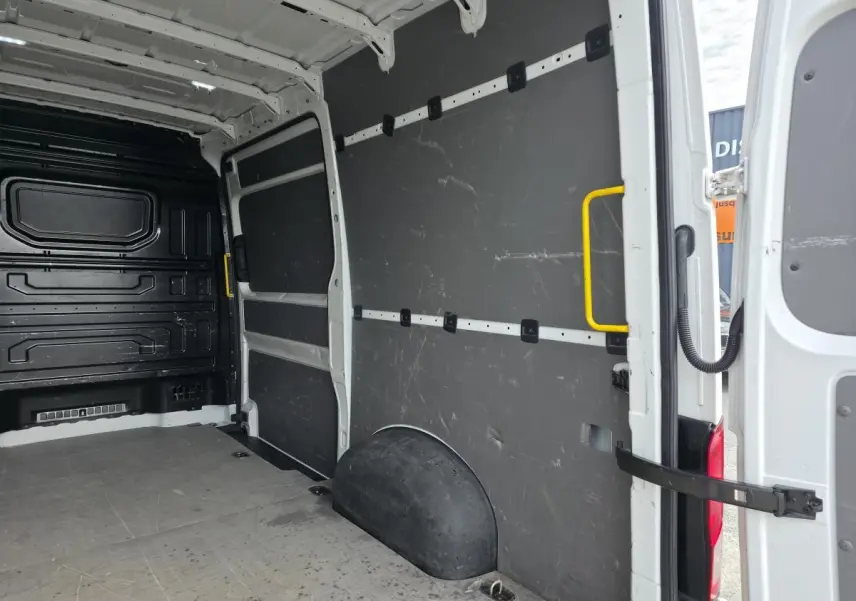 Vue intérieure arrière droite du Volkswagen Crafter blanc, montrant l'espace de chargement avec plancher bois et protections latérales noires.