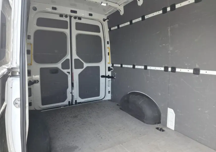 Vue intérieure arrière du fourgon Volkswagen Crafter blanc, montrant l'espace de chargement avec plancher et parois protégés.