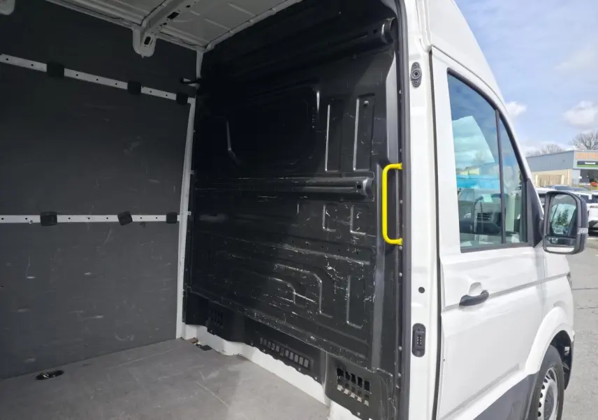 Vue intérieure arrière droite du Volkswagen Crafter blanc avec plancher bois et poignée jaune sur cloison de séparation.
