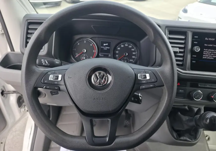 Vue intérieure centrée sur le volant noir Volkswagen et le tableau de bord du fourgon blanc Volkswagen Crafter 2023.