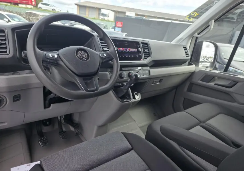 Vue intérieure côté conducteur du Volkswagen Crafter Fourgon blanc 2023, tableau de bord et volant multifonctions visibles.