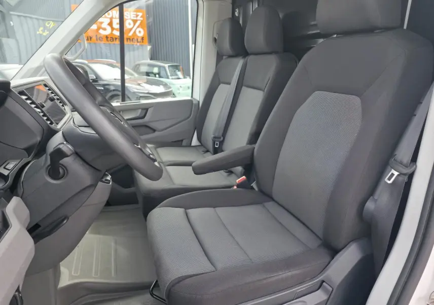 Vue intérieure côté conducteur du Volkswagen Crafter Fourgon blanc 2023, montrant les sièges tissu gris et le volant multifonctions.