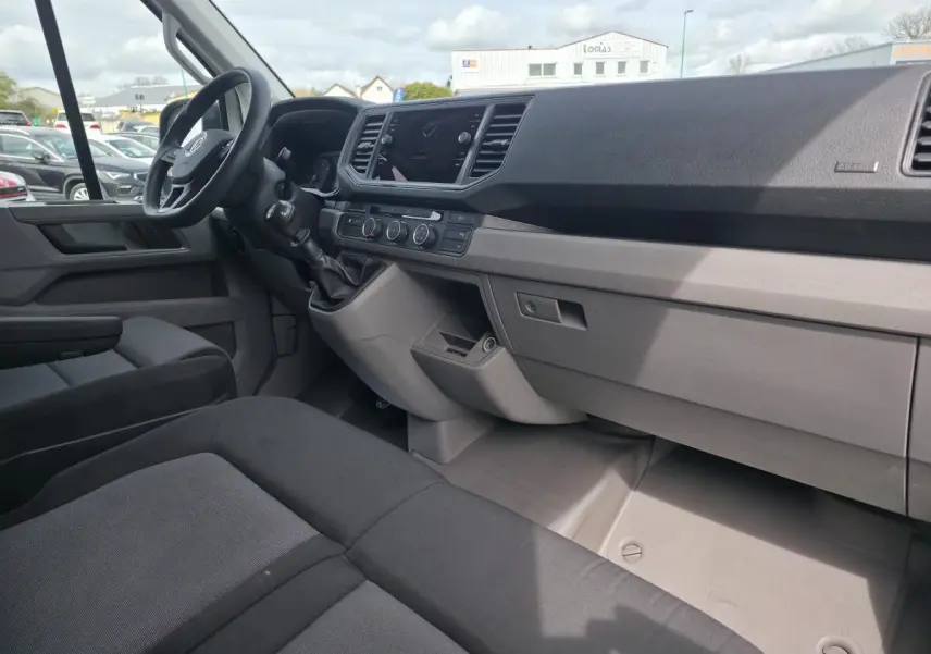 Vue intérieure côté conducteur du Volkswagen Crafter Fourgon 2023 avec tableau de bord gris et sièges tissu noirs.