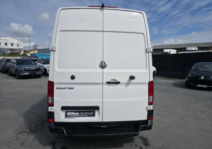 Vue arrière d’un Volkswagen Crafter fourgon blanc avec portes battantes et logo centré sous ciel partiellement nuageux.