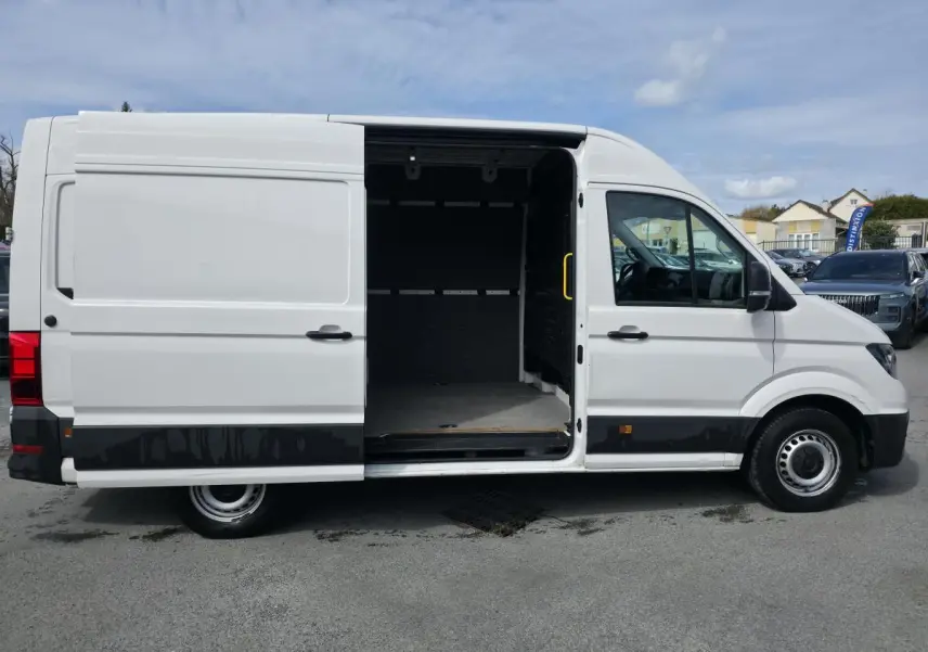 Vue latérale gauche d’un Volkswagen Crafter blanc avec porte coulissante ouverte montrant l’espace de chargement vide.