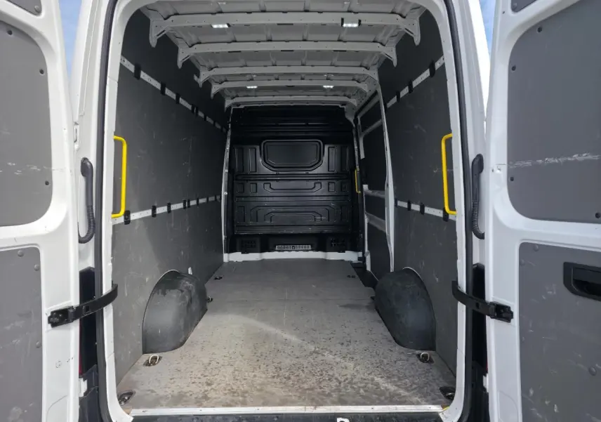 Vue intérieure arrière du Volkswagen Crafter blanc, montrant l'espace de chargement avec plancher bois et protections latérales grises.