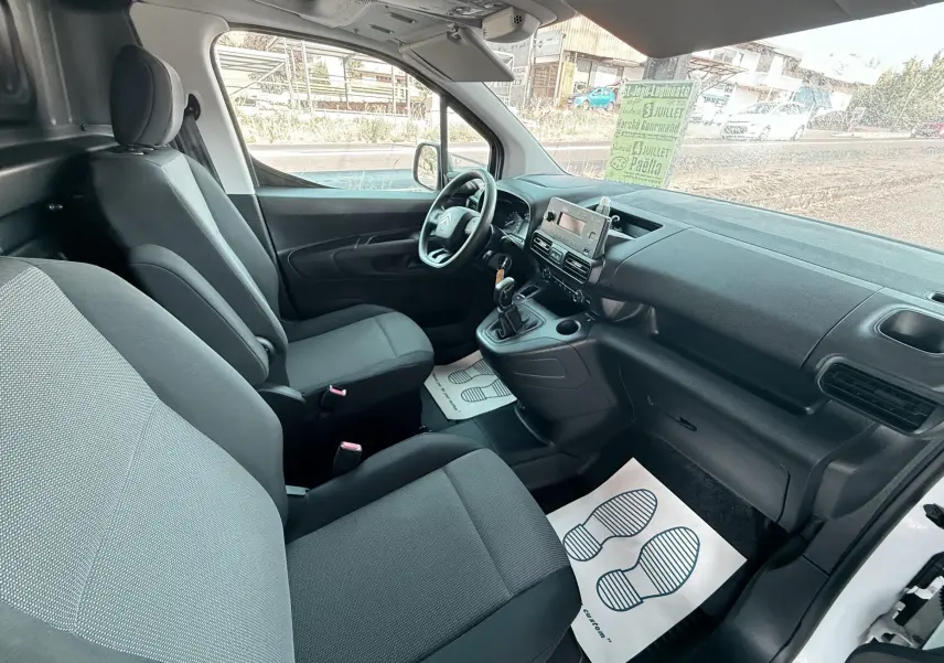 Vue intérieure côté conducteur du Citroën Berlingo blanc 2019, montrant les sièges avant et le tableau de bord avec boîte manuelle.