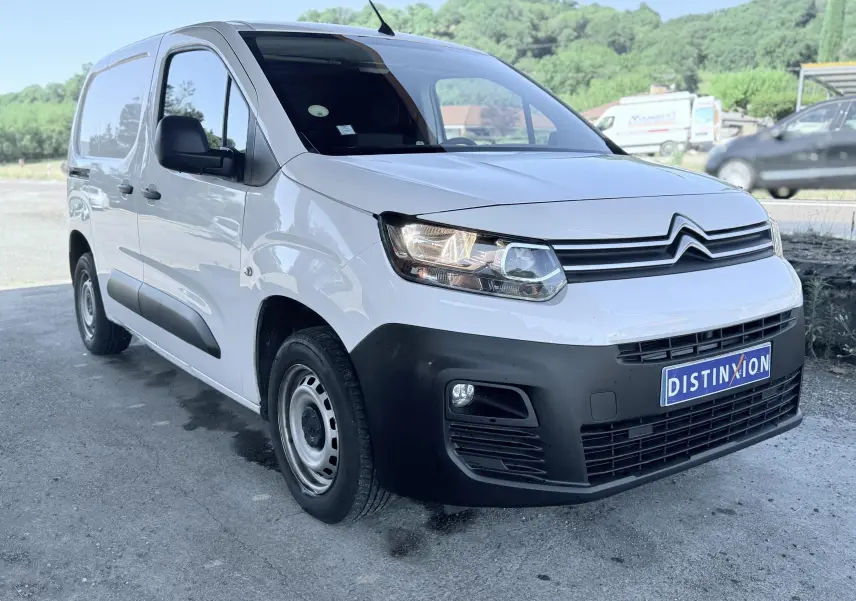 Vue 3/4 avant d’un Citroën Berlingo blanc avec pare-chocs noir mat et jantes acier grises sur parking extérieur.
