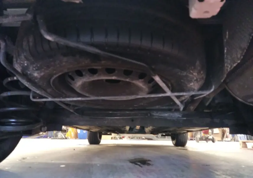 Vue sous le Renault Kangoo blanc 2019 montrant la roue de secours fixée sous le châssis et la suspension arrière.