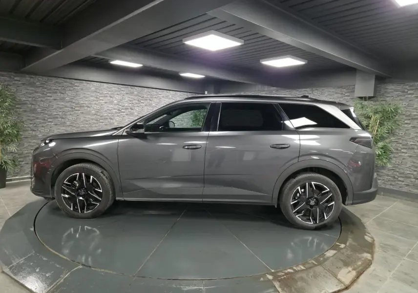 Vue latérale droite d'un Peugeot 5008 gris métallisé avec jantes alliage noires et barres de toit noires brillantes.