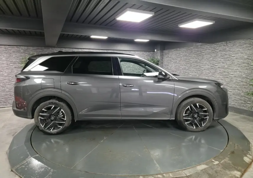 Vue de profil côté gauche d’un Peugeot 5008 gris métallisé avec jantes alliage 19 pouces et barres de toit noires.