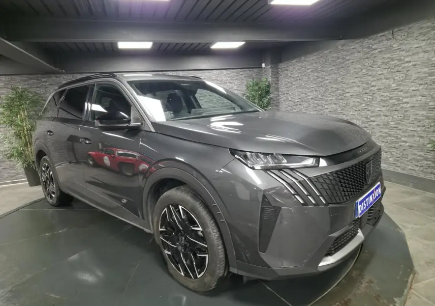 Vue 3/4 avant droite d’un Peugeot 5008 gris métallisé avec jantes alliage noires et calandre noire distinctive.