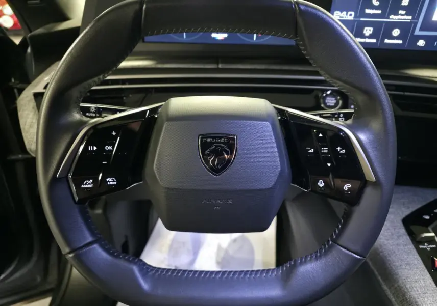 Vue rapprochée du volant noir cuir du Peugeot 5008 2025 avec commandes intégrées et logo central.