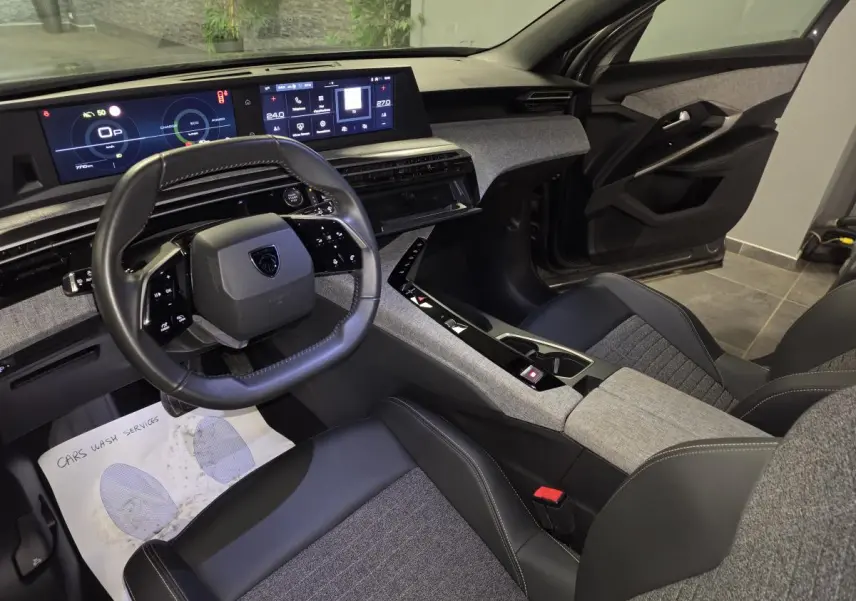 Vue intérieure côté conducteur du Peugeot 5008 2025, mettant en valeur le tableau de bord numérique et la sellerie tissu gris et cuir noir.