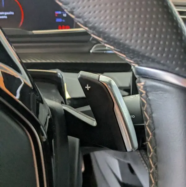 Gros plan sur la palette de changement de vitesse + du volant en cuir perforé dans la Peugeot 508 SW gris selenium 2024.