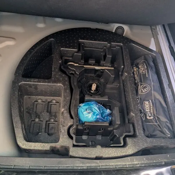 Compartiment de rangement sous le plancher du coffre du Peugeot 508 SW gris, avec trousse de secours et espace vide pour outils.