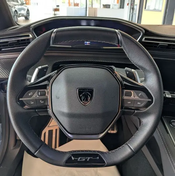 Volant cuir noir avec logo Peugeot et inscription GT au centre du tableau de bord d'une 508 SW gris selenium 2024.