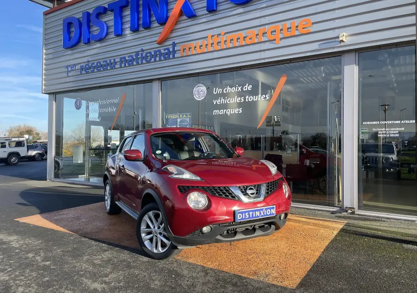 Nissan Juke rouge vue 3/4 avant droit devant un showroom avec plaque Distinxion visible.