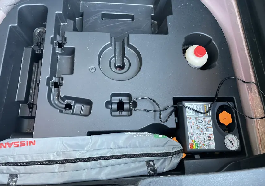 Vue plongeante sur le coffre du Nissan Juke rouge 2017, montrant le kit de réparation pneus et trousse de secours.