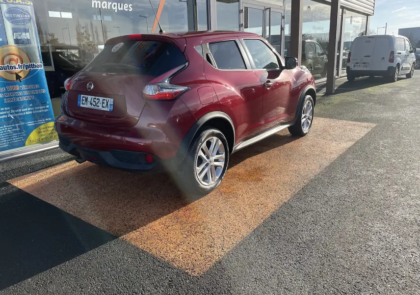 Nissan Juke rouge vue 3/4 arrière droit, stationné devant un bâtiment avec vitres réfléchissantes.