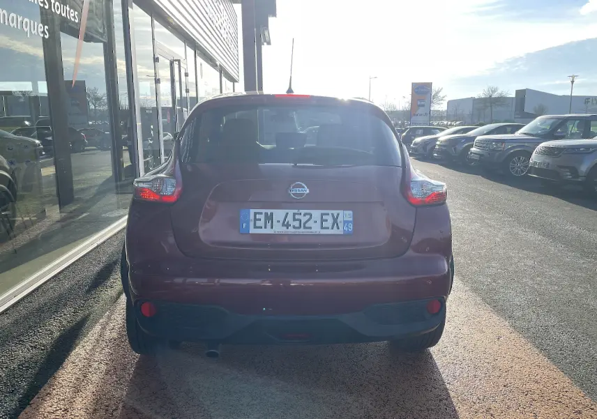 Vue arrière d'un Nissan Juke rouge 2017 garé devant une vitrine, avec feux arrière allumés et plaque visible.