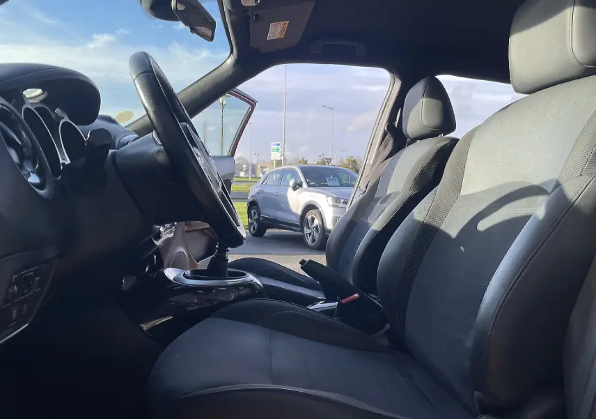 Vue intérieure côté conducteur du Nissan Juke rouge 2017, mettant en valeur les sièges gris-noir et la boîte manuelle.