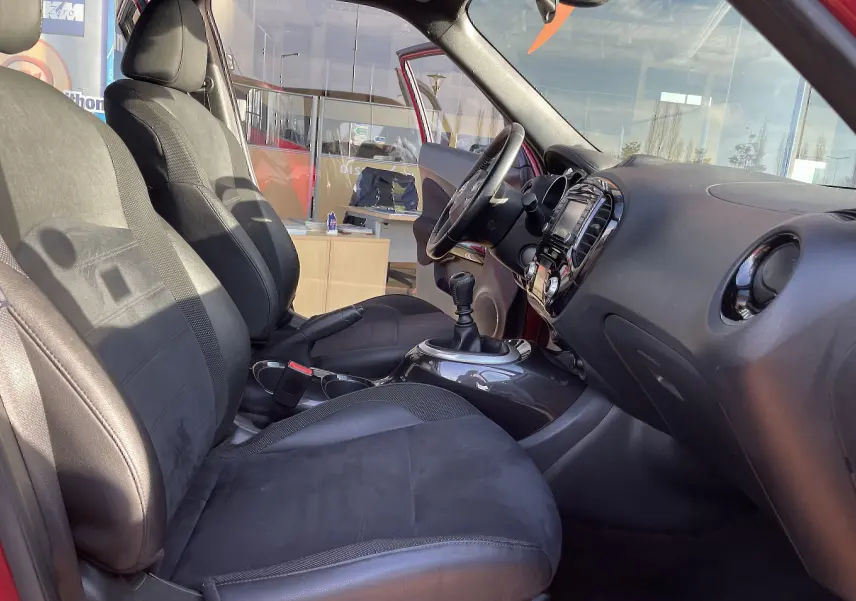 Vue intérieure côté conducteur du Nissan Juke rouge 2017, mettant en valeur les sièges noirs et la console avec levier de vitesse manuel.