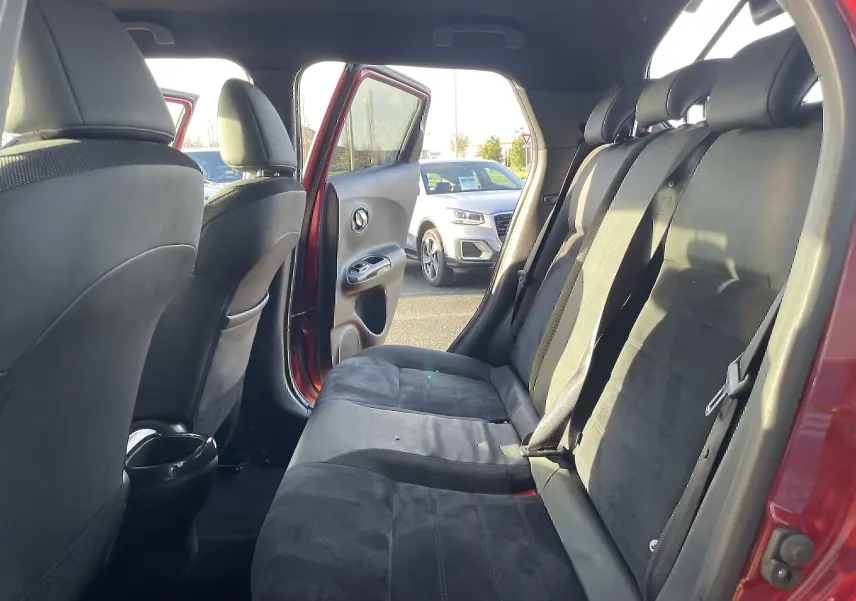Vue intérieure côté droit montrant la banquette arrière noire du Nissan Juke rouge avec porte arrière ouverte.