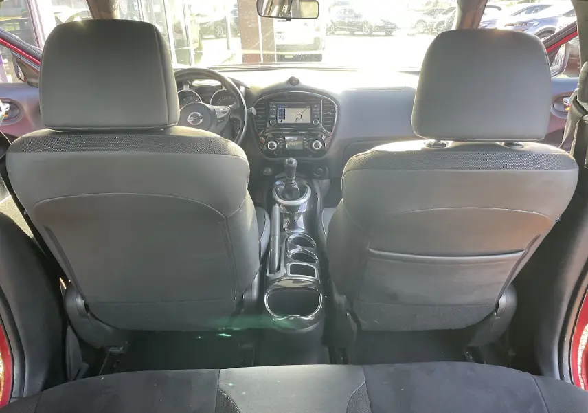 Vue intérieure arrière du Nissan Juke rouge 2017, mettant en valeur la console centrale avec boîte manuelle et écran GPS.